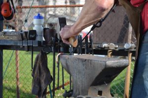 A man is working on an outdoor blacksmith 's tool.